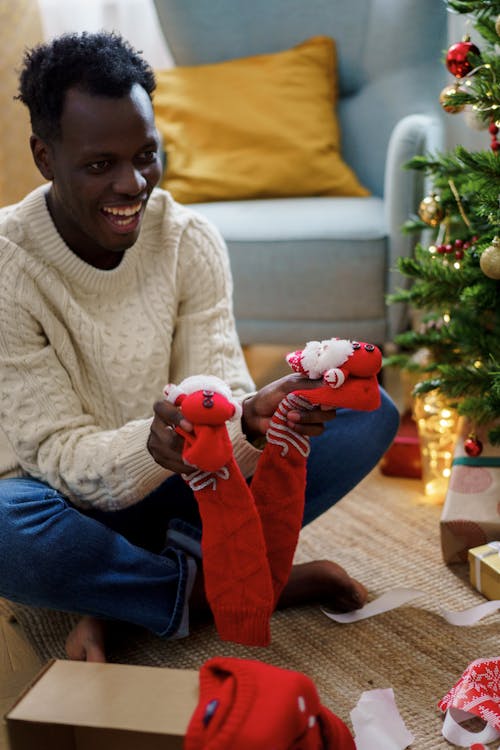 A Man in White Sweater Smiling While Holding a Red Christmas Socks