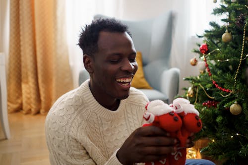 A Man in White Sweater Smiling While Holding a Red Christmas Socks