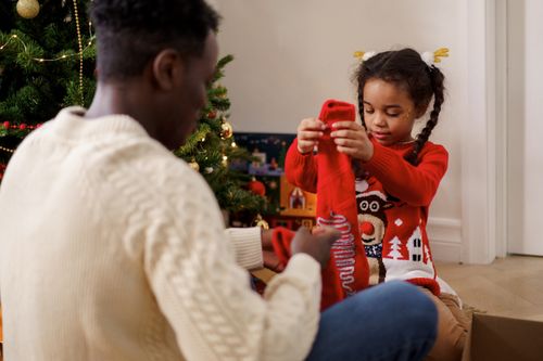 Free Joyful father and daughter unboxing a Christmas gift by the tree at home. Stock Photo