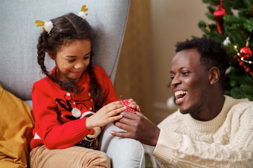 Free A joyful father and daughter exchange gifts by the Christmas tree, sharing heartwarming holiday moments. Stock Photo