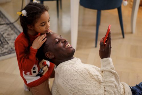 Free Father and daughter enjoy Christmas time with joyful smiles and a smartphone indoors. Stock Photo