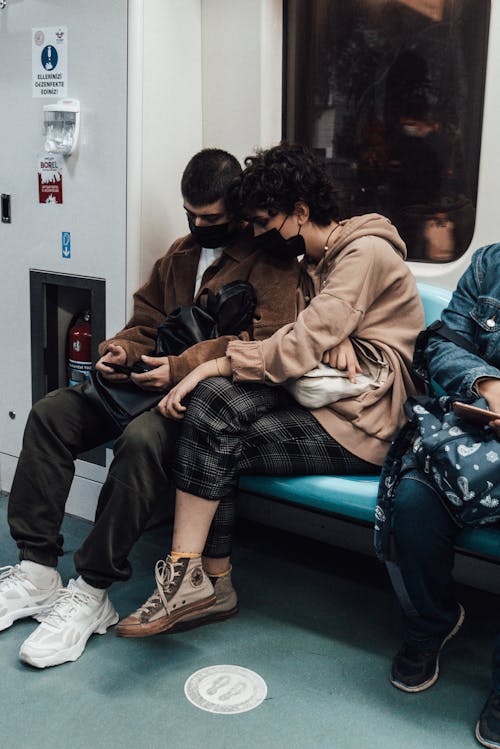 Free Unrecognizable young ethnic couple in trendy outfits and face masks using smartphone while riding modern subway train Stock Photo