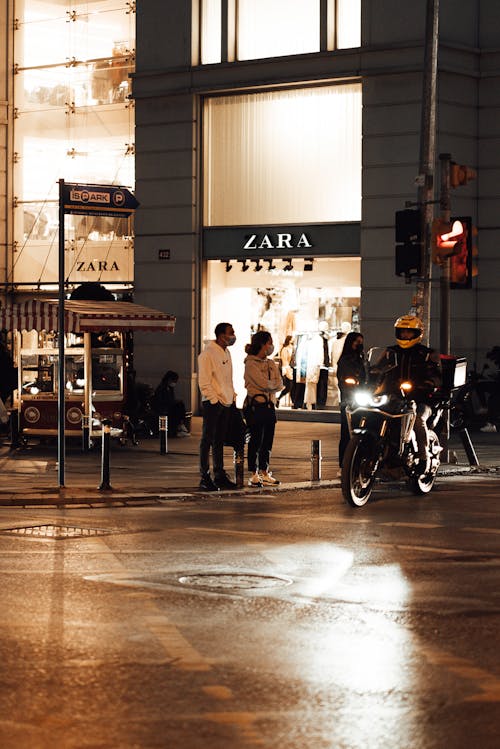 Unrecognizable pedestrians standing near traffic light in modern city in evening