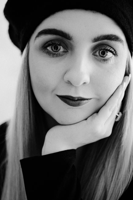 Elegant black and white portrait of a woman with hand on face wearing a hat.