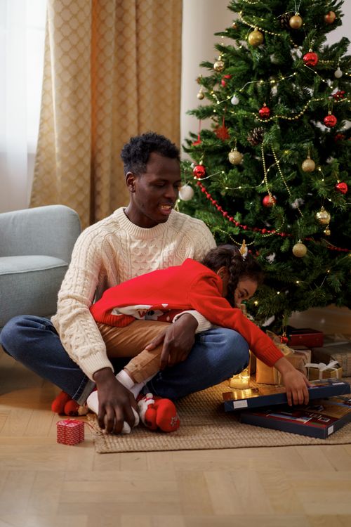Free A joyful father and daughter celebrating Christmas morning by the tree filled with gifts and festive cheer. Stock Photo