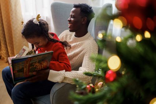 Free A joyful father and daughter share a magical storytime next to a festive Christmas tree indoors. Stock Photo