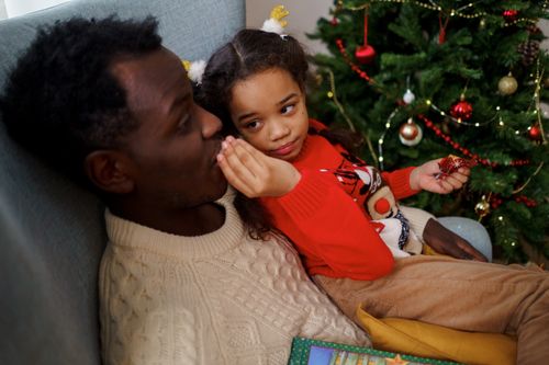 Free Father and daughter sharing a tender moment by the Christmas tree, enjoying the festive atmosphere. Stock Photo