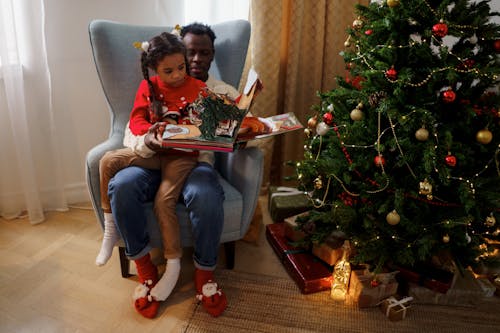 Dad and Daughter Reading a Fairy Tale Book While Sitting Beside a Christmas Tree