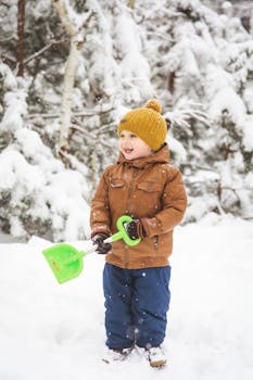 Joyful child in winter gear holding a shovel in a snowy outdoor setting.