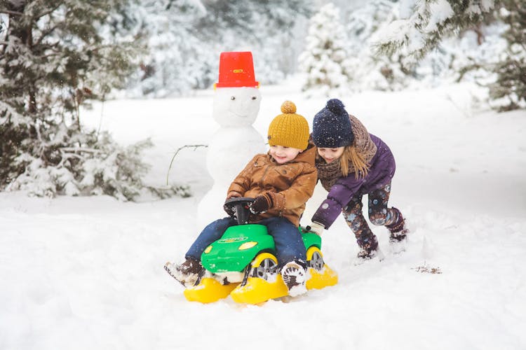 A Girl Pushing A Boy On A Plastic Toy Car