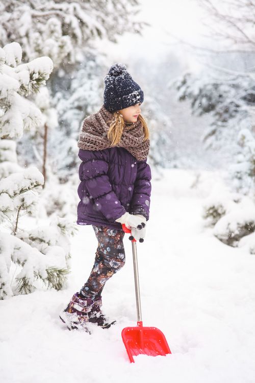 Free A young girl dressed warmly shoveling snow in a beautiful winter setting. Stock Photo
