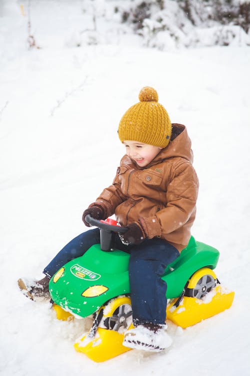 A Boy Riding a Green Plastic Toy Car on Snow Covered Ground