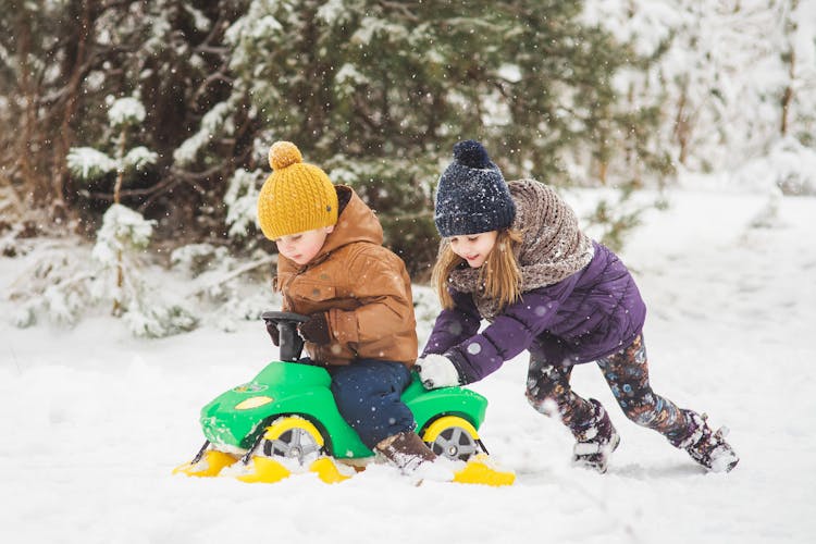 A Cute Girl Pushing A Boy On A Plastic Toy Car