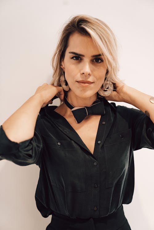 Confident young woman adjusting bow tie in studio