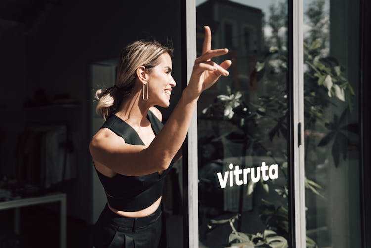 Smiling Woman Waving Hand Near Entry Of Shop