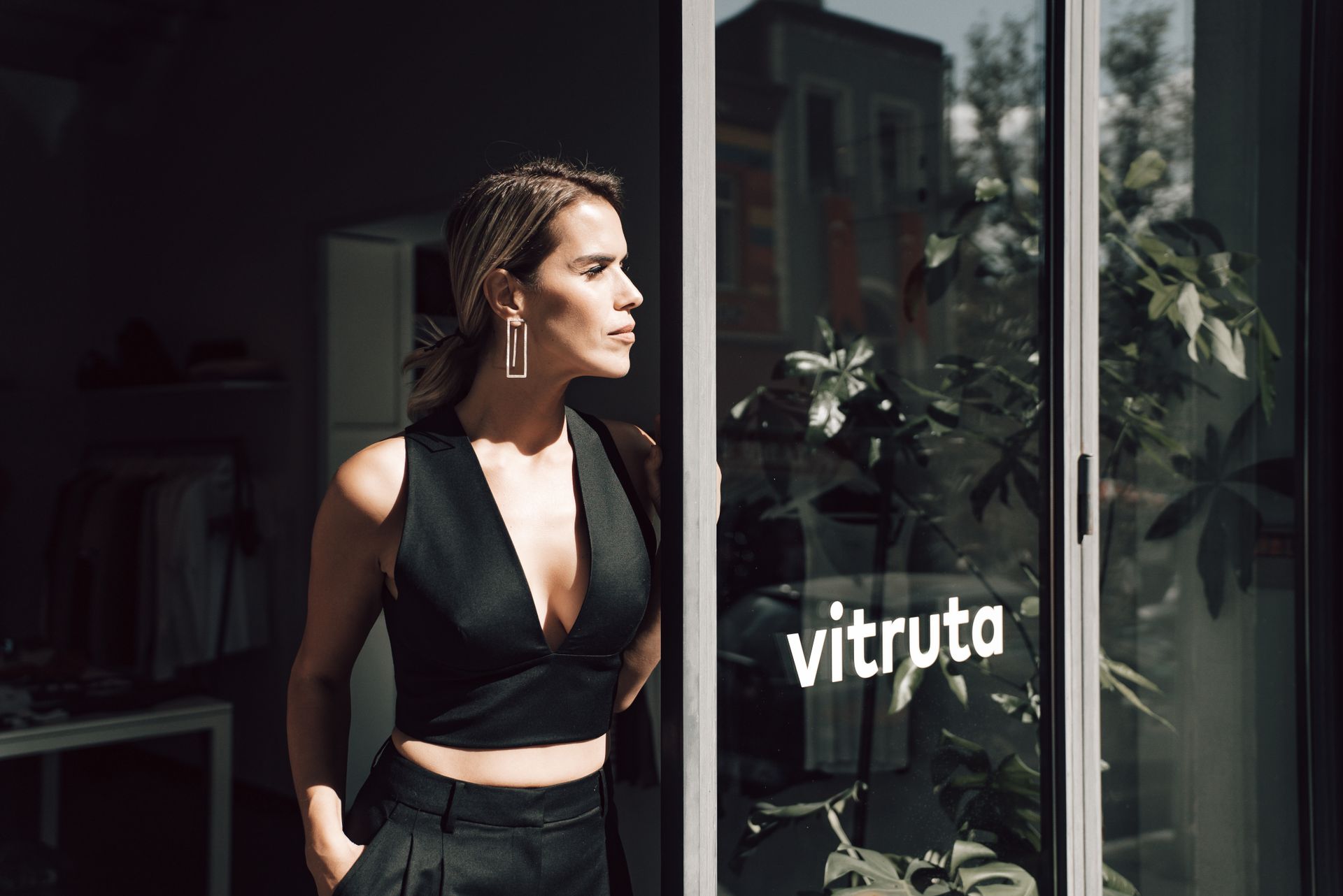 Serious female entrepreneur in trendy outfit standing near glass doorway of store and looking away