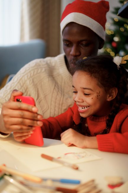 Father and daughter share a joyful moment taking a selfie during the festive season indoors.