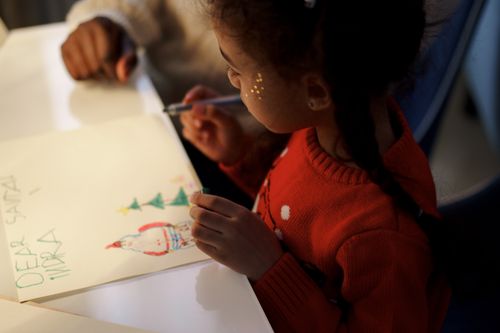 Free A young girl in a red sweater writing a letter to Santa, capturing holiday creativity indoors. Stock Photo