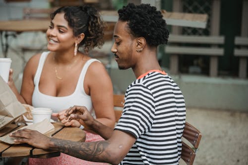Free Happy young Hispanic woman and African American man in casual clothes resting on cafe terrace and drinking takeaway coffee during date Stock Photo