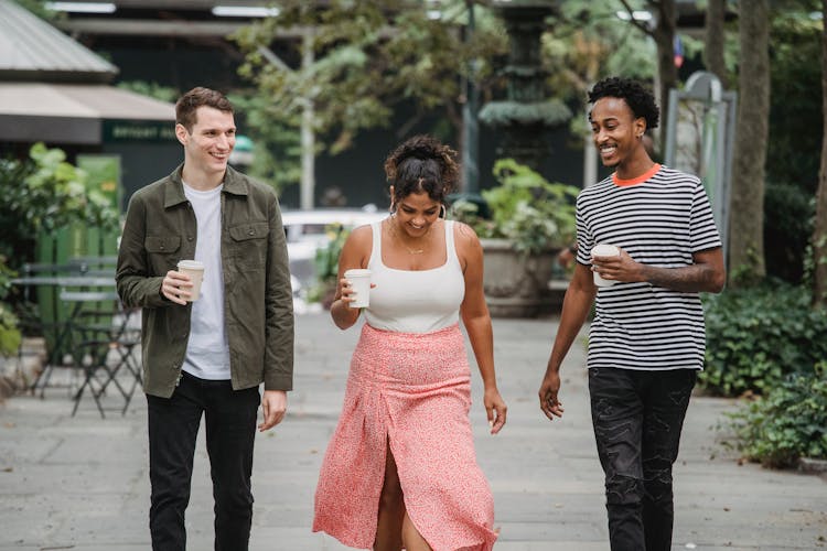 Joyful Young Diverse Friends Walking In Park And Smiling With Coffee To Go