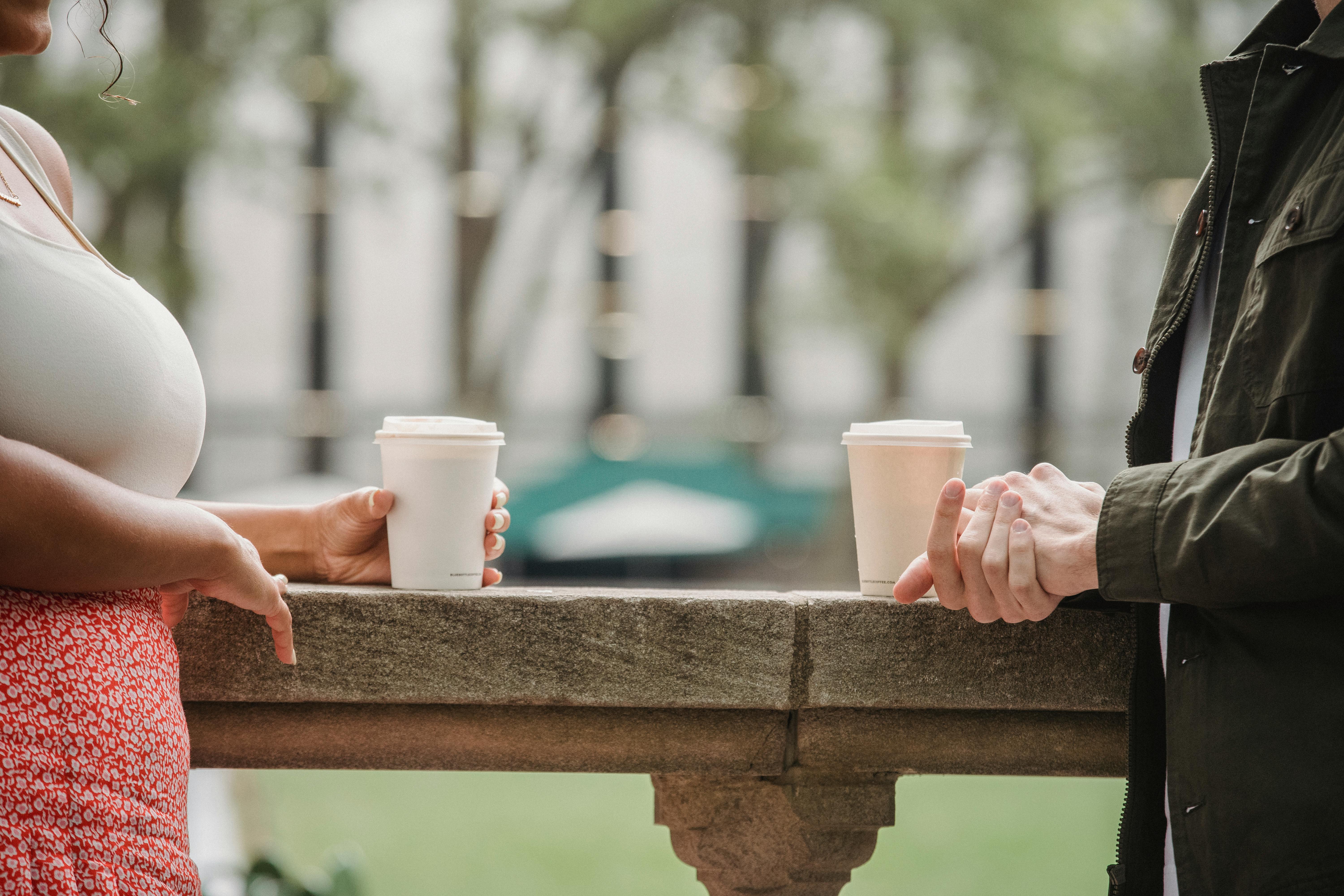 faceless young couple drinking takeaway coffee on terrace