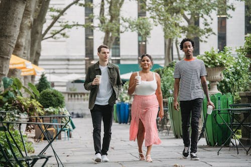 Free Trendy diverse students walking in park and enjoying takeaway coffee Stock Photo