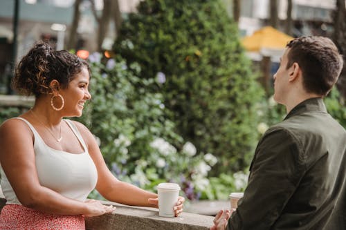 Free Cheerful young Hispanic woman in casual clothes with boyfriend standing on terrace and smiling while having coffee break together in outdoor cafe Stock Photo