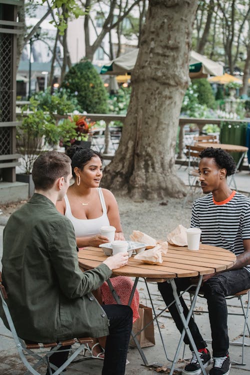 Free From above of young multiracial friends chatting at table in park cafe with takeaway coffee and snacks on sunny day Stock Photo