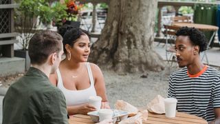 Young multiracial friends chatting over takeaway coffee at a park cafe