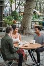 From above of young multiracial friends chatting at table in park cafe with takeaway coffee and snacks on sunny day