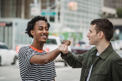 Free Cheerful young diverse male friends in casual clothes bumping arms and smiling while greeting each other on modern city street Stock Photo