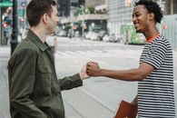 Joyful young multiethnic guys shaking hands on city street