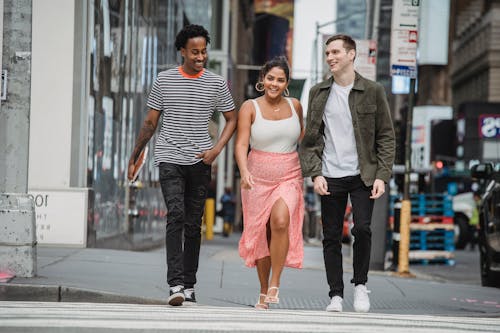 Full length of cheerful young multiracial male and female friends in stylish clothes walking on zebra crossing while spending time together in city
