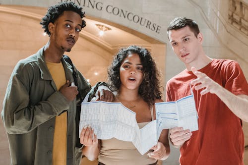 Free Amazed young multiracial male and female friends in casual outfits looking away while exploring map in Grand Central Terminal Stock Photo