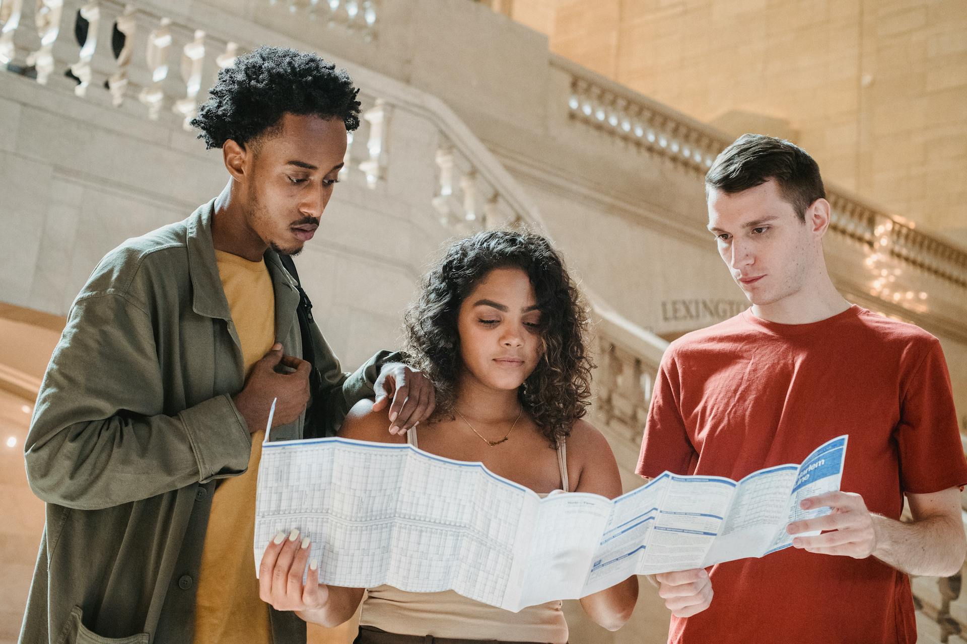 Serious young diverse millennials reading map in railway station terminal