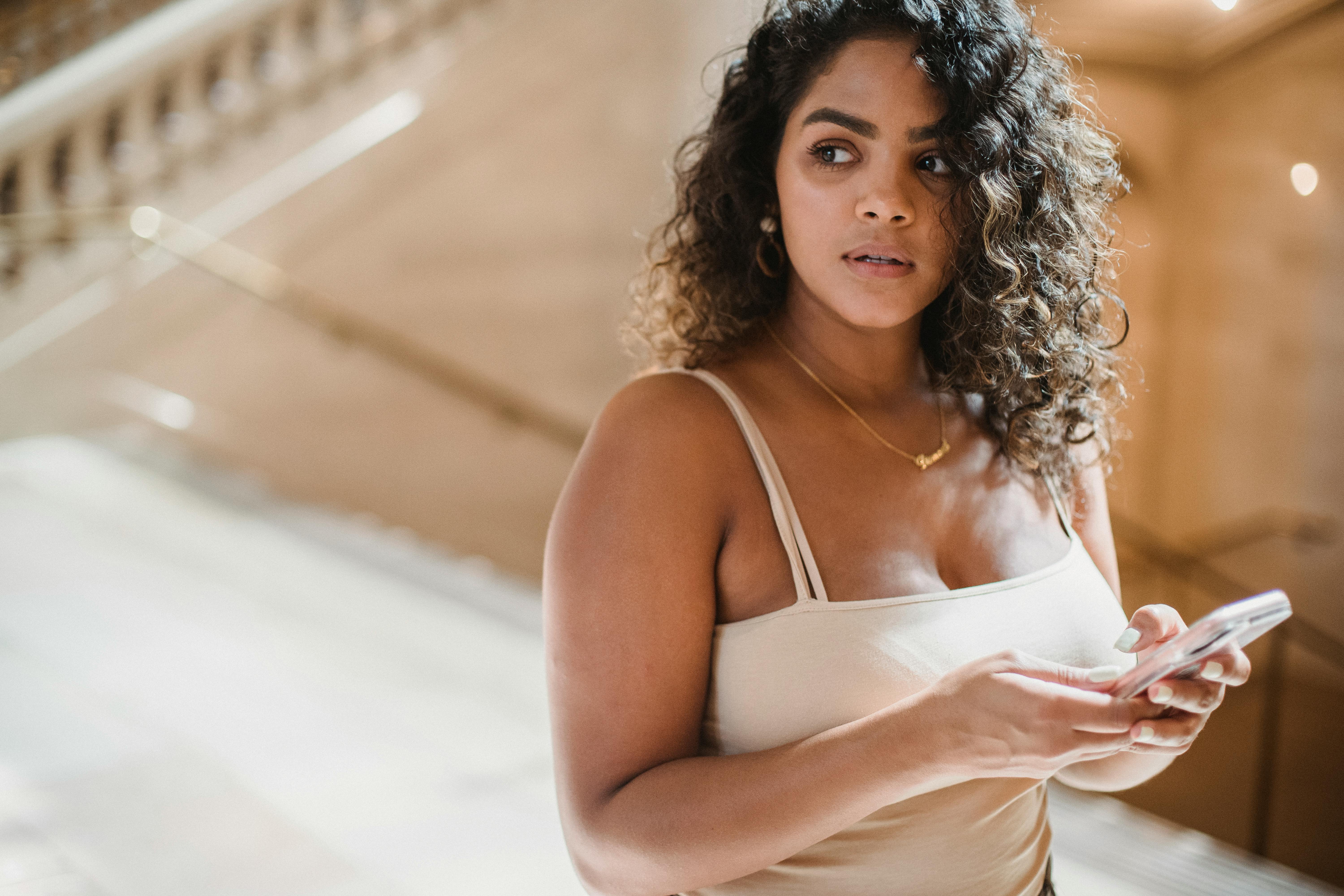 serious young ethnic woman using smartphone in hallway of aged building