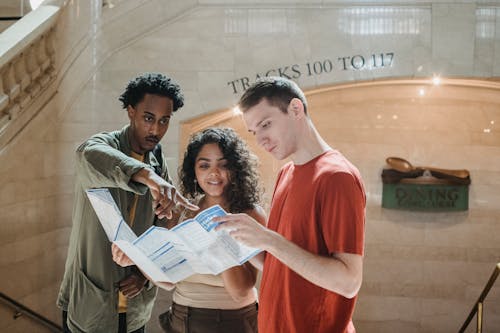 Young focused diverse students exploring map in railway station