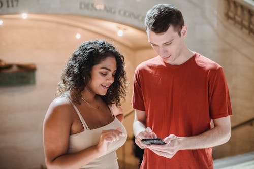 Positive young diverse students surfing smartphone in hallway