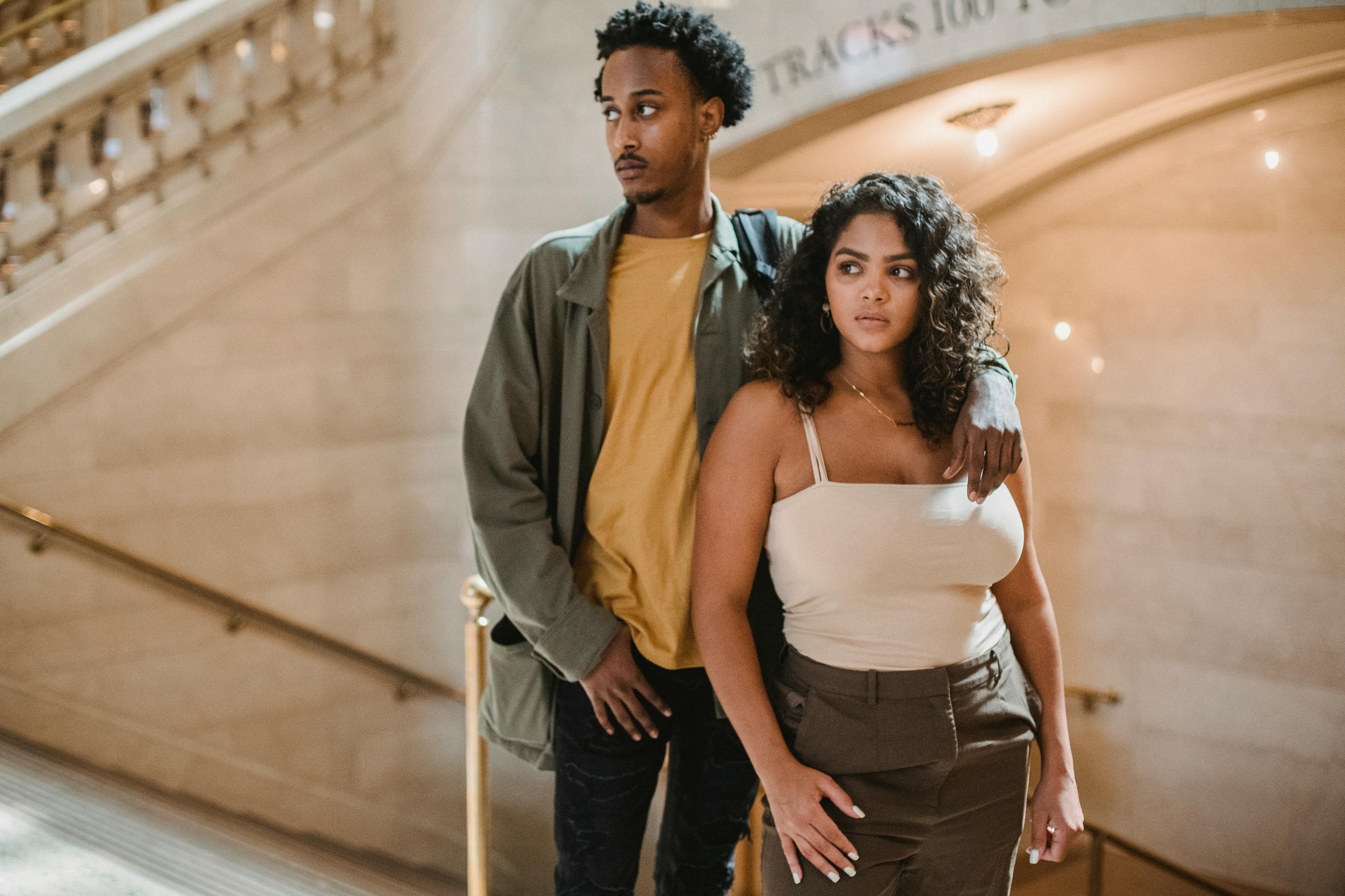Concentrated young African American man in casual clothes hugging Hispanic girlfriend while standing together in corridor of old building