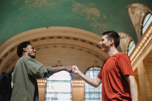 Cheerful young multiracial male friends bumping fists in old building