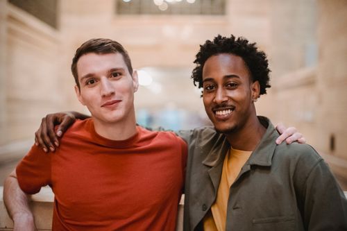 Free Joyful multiracial male friends looking at camera and embracing while standing near stone barrier in modern building on blurred background Stock Photo