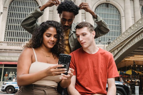 Free Focused multiethnic friends browsing smartphone on street Stock Photo