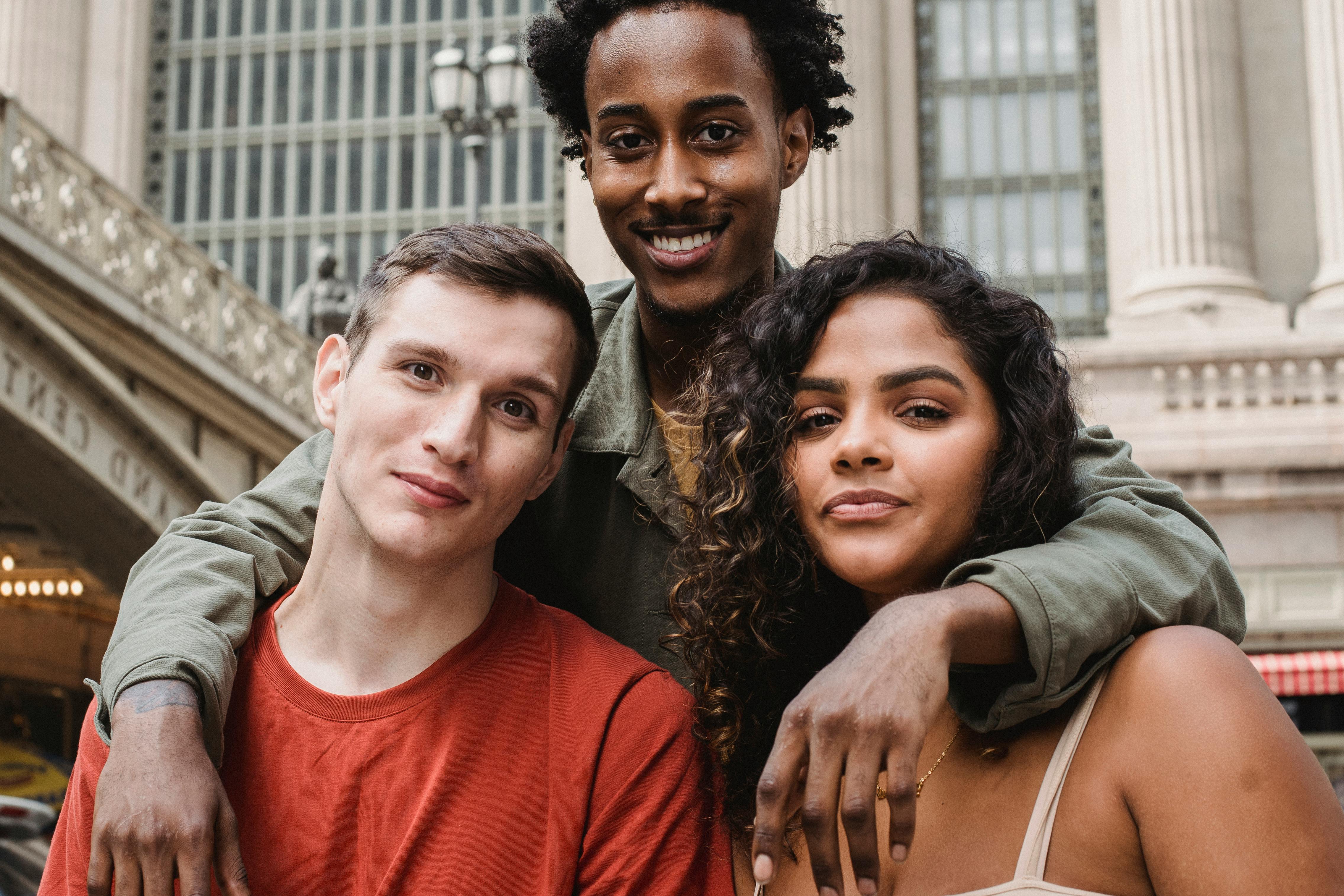 positive black guy hugging smiling multiracial friends near urban building