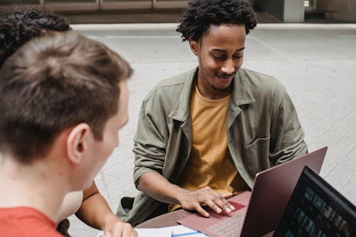 Free From above of positive young multiracial students discussing project details while browsing laptops together and sitting in outdoors cafeteria Stock Photo