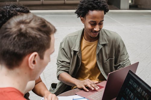 From above of positive young multiracial students discussing project details while browsing laptops together and sitting in outdoors cafeteria