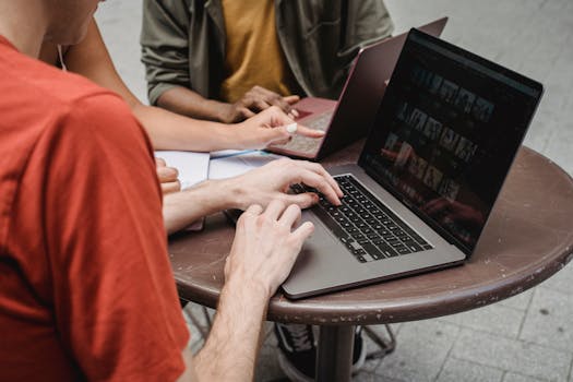 Group of young adults using laptops for teamwork at an outdoor café.