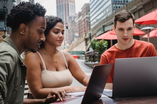 Focused young man using laptop while studying with diverse friends in outdoors cafeteria