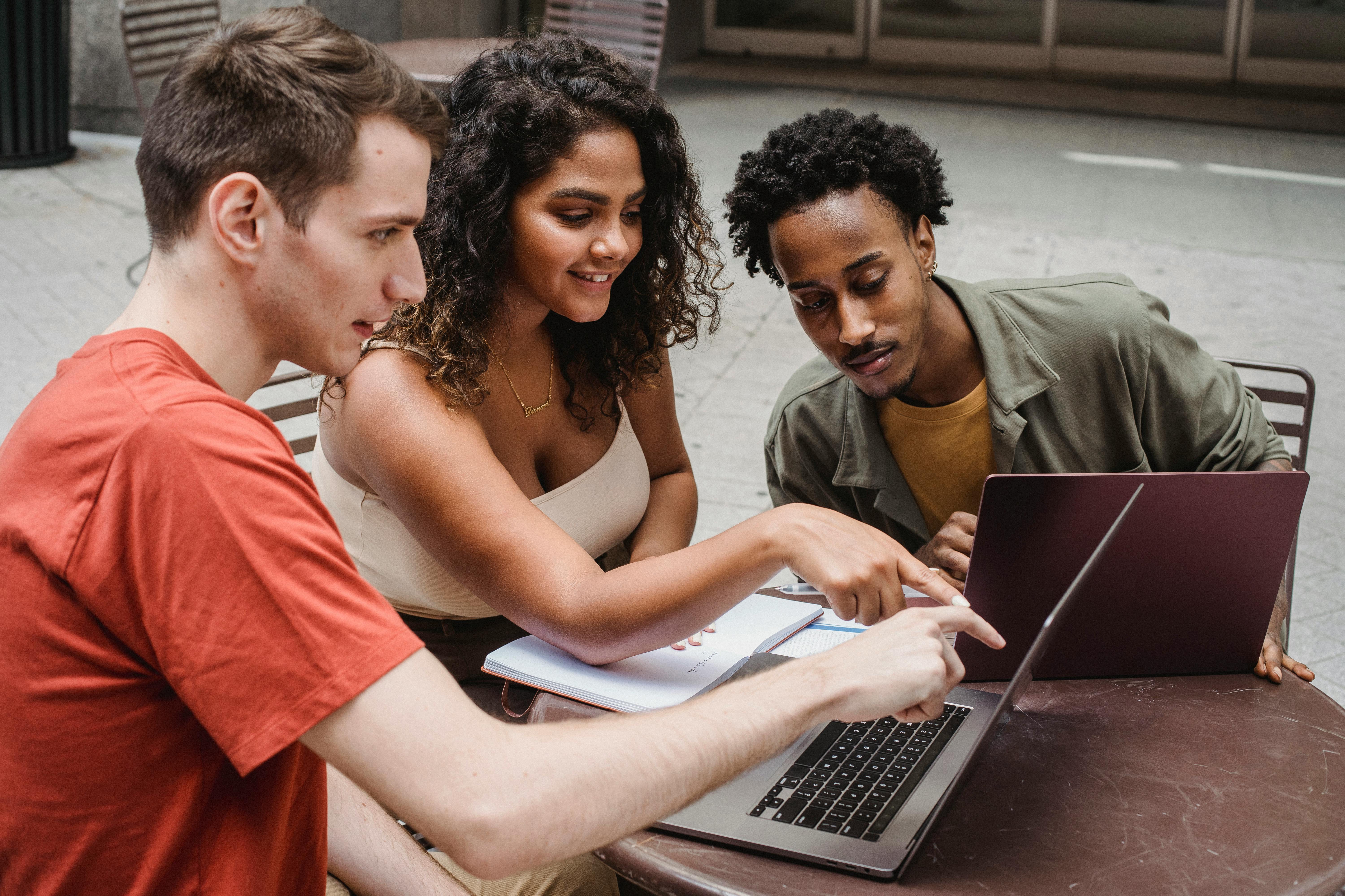 multiethnic students showing information on laptop to black man sitting in cafe