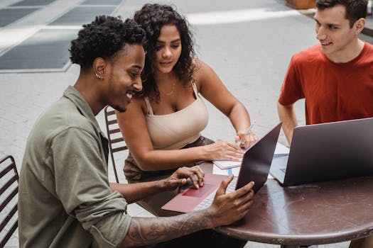 From above group of delightful diverse friends wearing casual clothes witting at round table in cafeteria and watching video on laptop in daytime