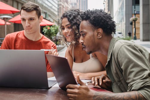 Free Concentrated young multiracial students sitting in street cafe and using laptops while preparing for exams on sunny day Stock Photo